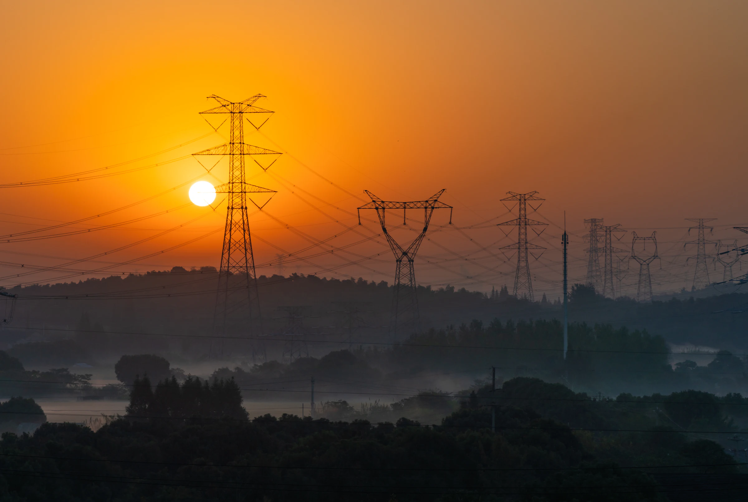 Strommasten über nebligen Hügeln bei Sonnenaufgang